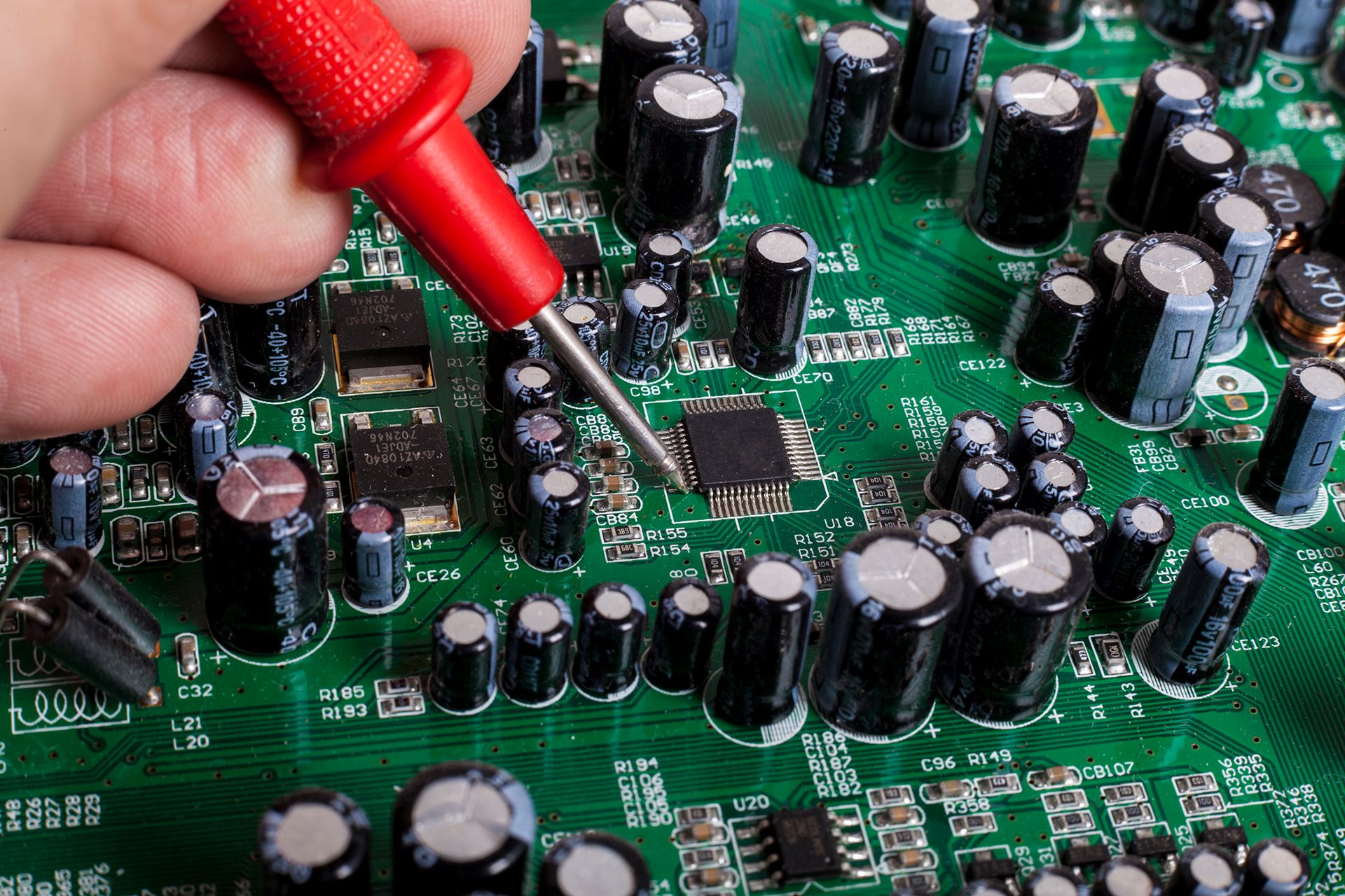 Electronics Repair service close-up with red probe and capacitors on electronic board